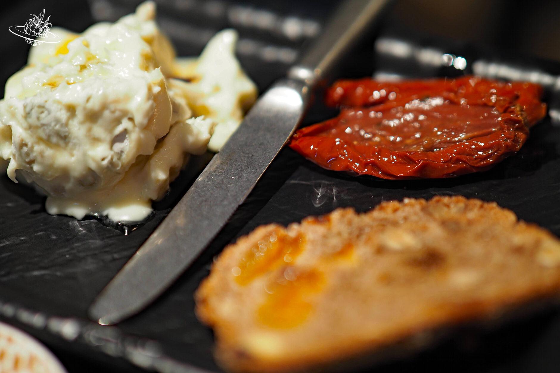 Schwarze Platte mit Gorgonzola, eingelegten Tomaten und einer Scheibe Früchtebrot