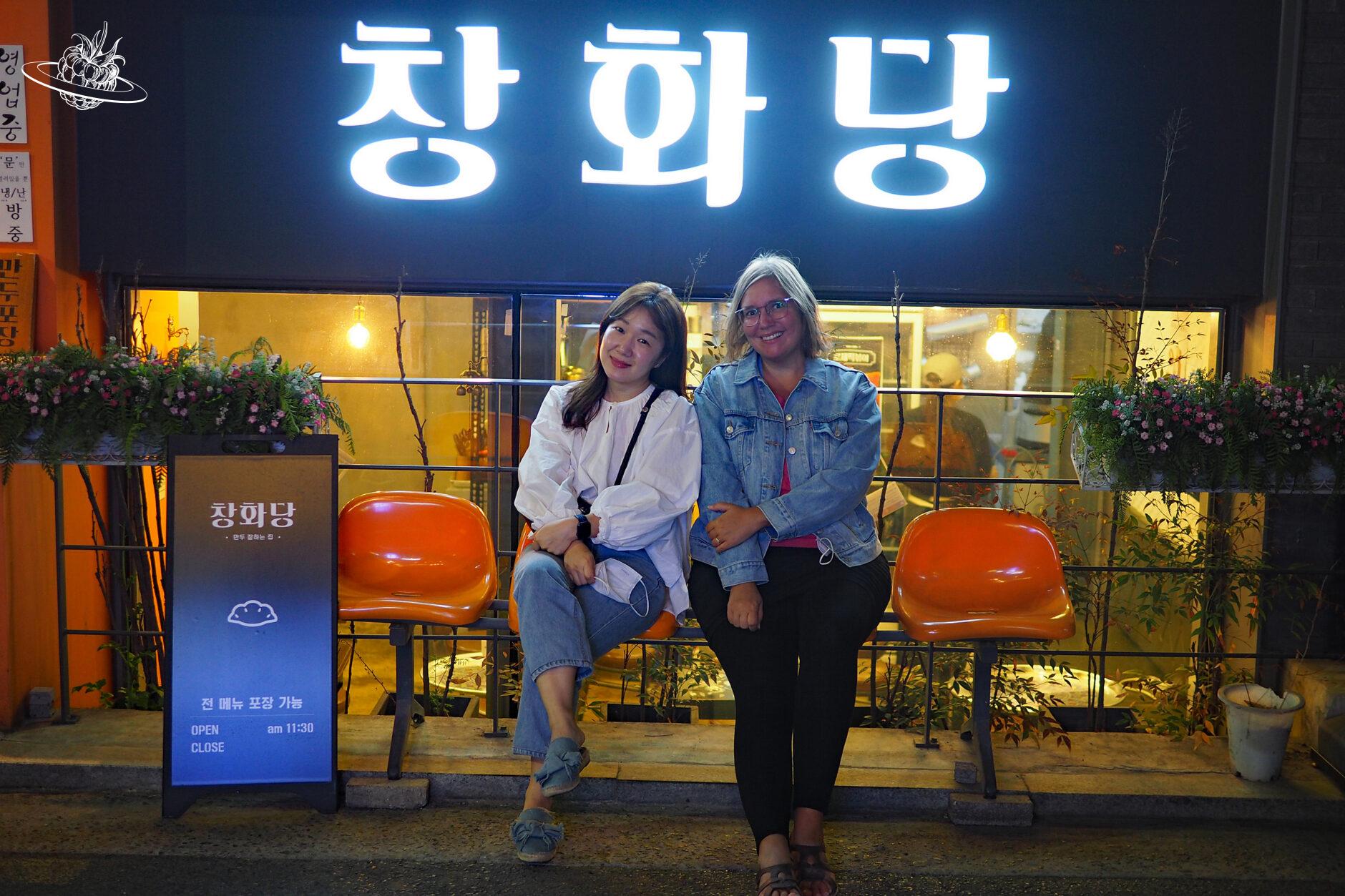 zwei frauen sitzen auf einer bank vor einem koreanischen restaurant