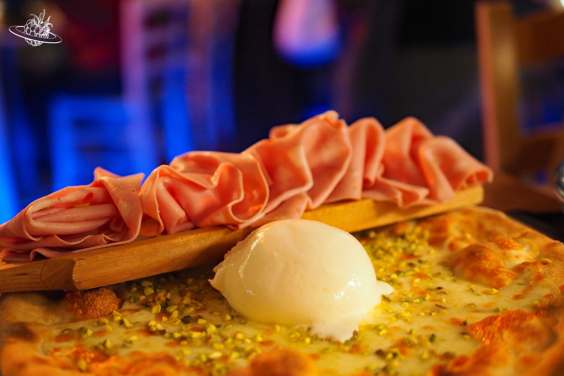 Auf einer Pizza liegt Burrata und auf einem Holzbrett liegt Mortadella