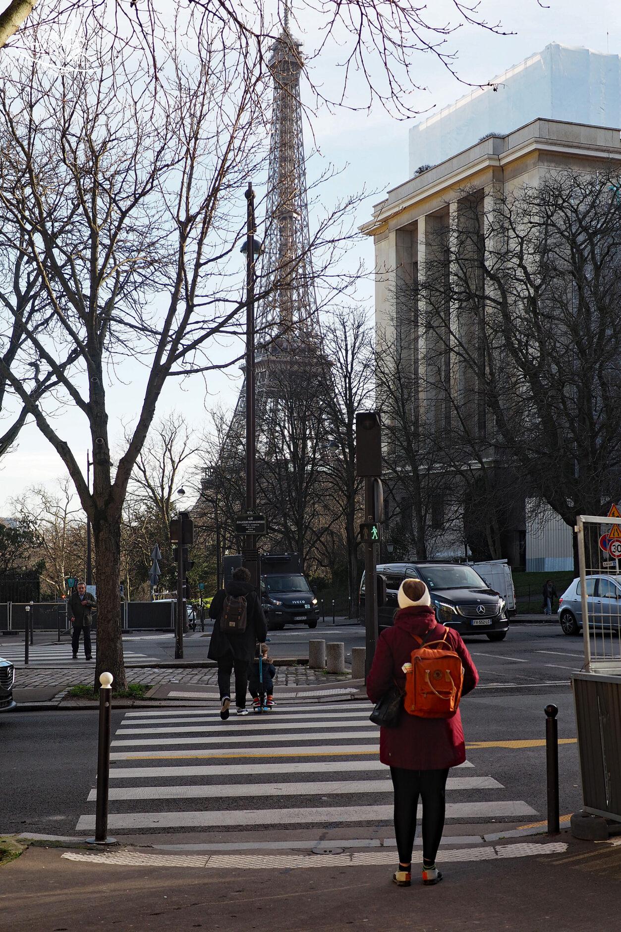 Frau geht über die Strasse und im Hintergrund ist der Eiffelturm