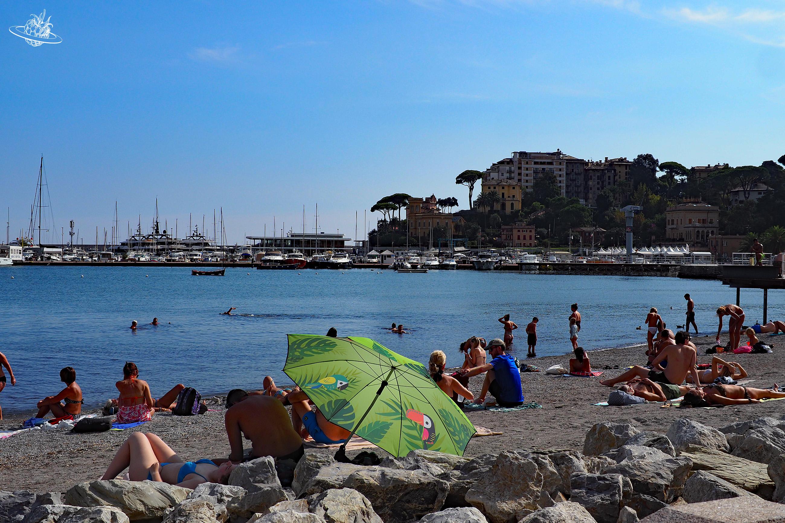 Badestrand mit vielen Leuten und Hafen im Hintergrund