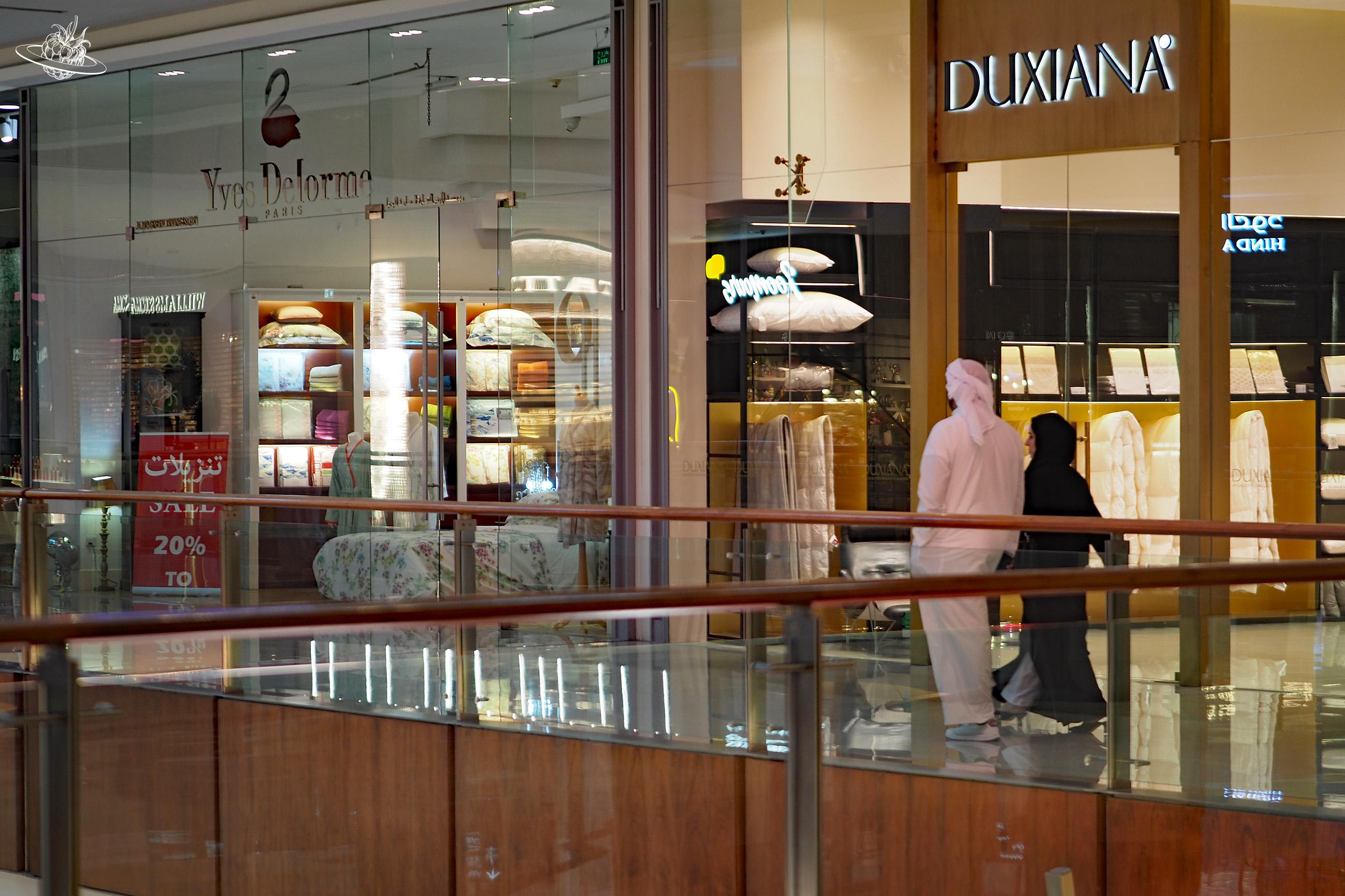 Zwei Emirati laufen durch die Dubai Mall an Möbel, Kleidern und Essenständen vorbei